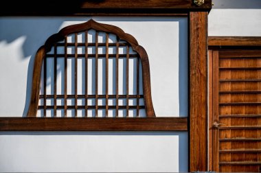 Ahşap pencere çerçevesi beyaz duvardaki ahşap kapının yanında.