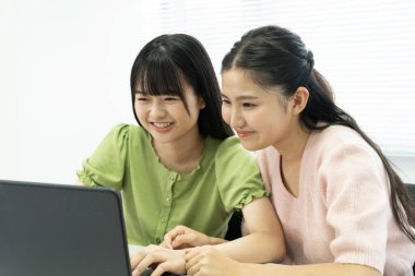 İki genç Asyalı kadın dizüstü bilgisayar kullanıyor ve birlikte eğleniyorlar. 