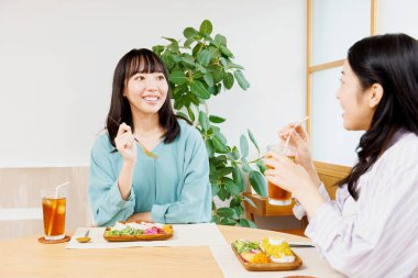 İki genç Japon kadın restoranda yemek yiyor.