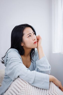 Düşünceli genç Asyalı kadın yatakta oturuyor.