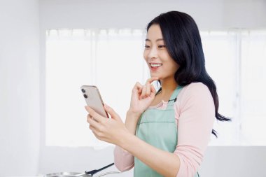 Asyalı kadın mutfakta akıllı telefon kullanıyor..