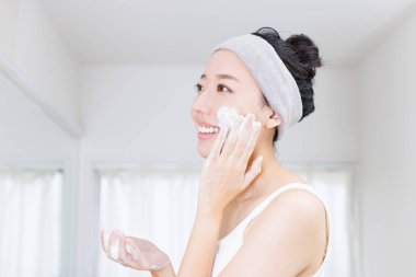 Genç Asyalı kadın yüzüne nemlendirici krem sürüyor. Evde cilt bakımı