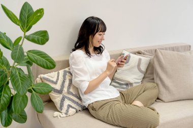 Evdeki koltukta cep telefonu gevşetici kullanan Asyalı genç bir kadın.
