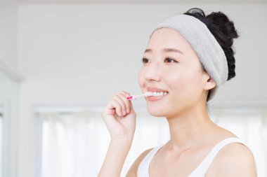 Mutlu Asyalı kadın dişlerini fırçalıyor.