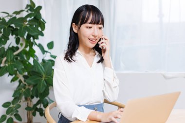 Asyalı kadın ev telefonunda dizüstü bilgisayar kullanıyor ve konuşuyor. 