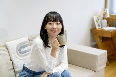 Oturma odasında oturan ve sıcak çay içen güzel genç bir Japon kadın. 