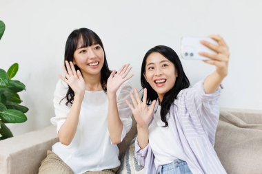 İki genç Asyalı kadın cep telefonuyla selfie çekiyor..