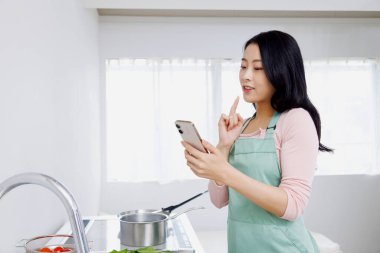 Asyalı kadın mutfakta akıllı telefon kullanıyor..