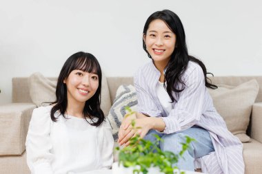 İki güzel Asyalı kadın evde otururken gülümsüyor.