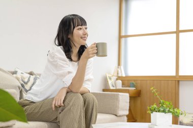 Oturma odasında oturan ve sıcak çay içen güzel genç bir Japon kadın. 