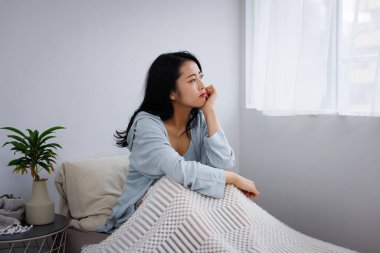 Düşünceli genç Asyalı kadın yatakta oturuyor.