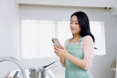 Asyalı kadın mutfakta akıllı telefon kullanıyor..