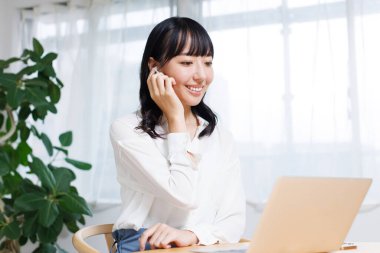 Genç Asyalı iş kadını modern ofiste dizüstü bilgisayar ve kulaklık kullanıyor. 