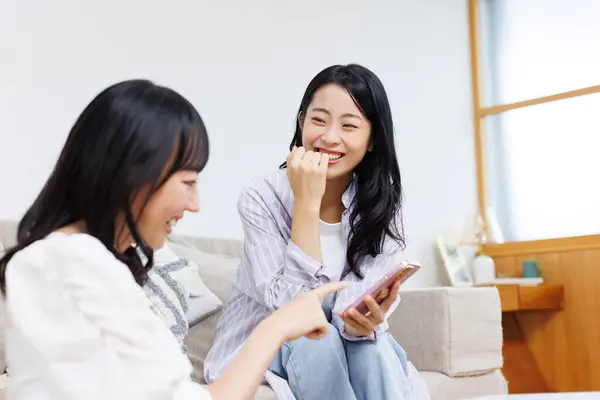 Akıllı Telefonlu Gülümseyen Asyalı Kadınlar Oturma Odasında Sohbet Ediyorlar — Stok fotoğraf