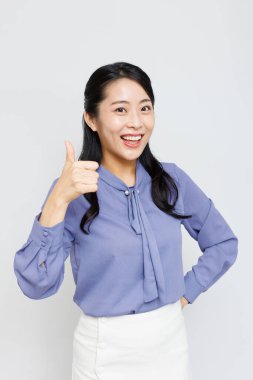 Tebessüm eden Asyalı kadın beyaz arka planda parmak gösteriyor.