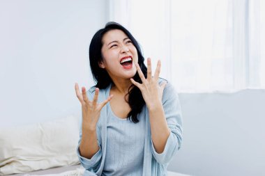 Asyalı, genç, mutlu bir kadın. Elleri yatak odasında, kanepede oturuyor. Heyecanlı..