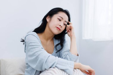 Asyalı genç kız yatakta oturuyor ve kafasına dokunuyor.