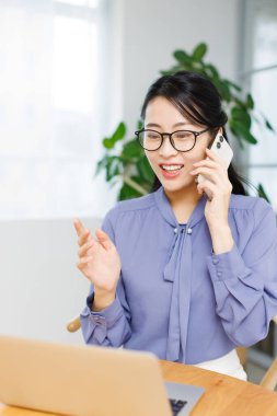 Genç Asyalı iş kadını ofiste akıllı telefon kullanıyor..