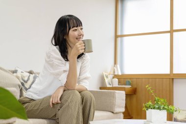 Oturma odasındaki kanepede oturan çay içen kadın.