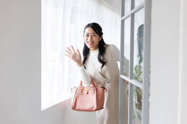 Pembe çantalı güzel Asyalı kadın evden çıkarken elini sallıyor.