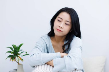 Genç Asyalı bir kadın, üzgün bir ifadeyle sabahleyin yatakta oturuyor.