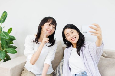 İki güzel Asyalı kadın evde selfie çekiyor.