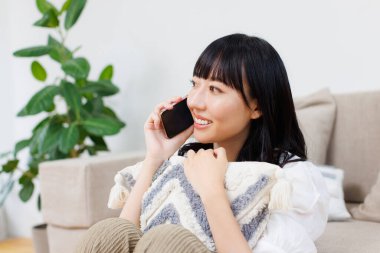 Genç, güzel Asyalı kadın evde cep telefonuyla konuşuyor.