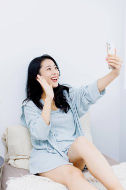 Asyalı bir kadın yatakta akıllı telefonuyla fotoğraf çekiyor.