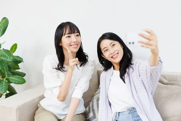 happy young asian women taking selfie with smartphone in living room. asian woman taking photo of her friends with camera and taking pictures at home.