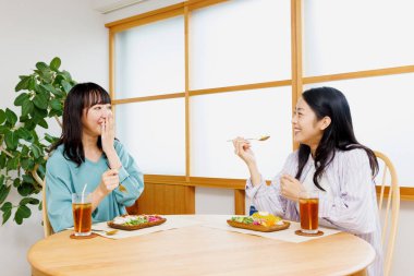 İki genç Japon kadın restoranda yemek yiyor.