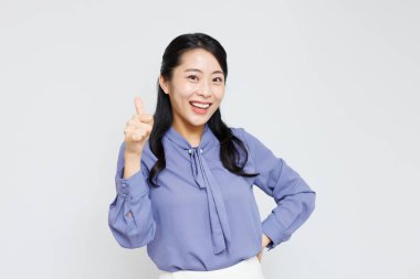 Mutlu gülümseyen Asyalı kadın kamerayı işaret ediyor, beyaz arka planda duruyor.
