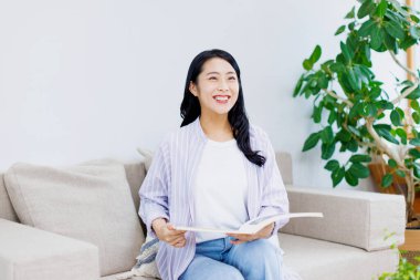 Asyalı kız üniversite öğrencisi evde kitap okuyor.