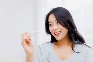 Gülümseyen Japon kadın evde hamilelik testine bakıyor.