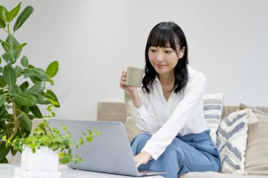 Dizüstü bilgisayarı ve bardağıyla koltukta oturan bir kadın.