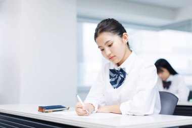 Okul üniforması giymiş, çağdaş bir sınıf ortamında ders çalışmaya odaklanmış çekici bir Japon kızın portresi..