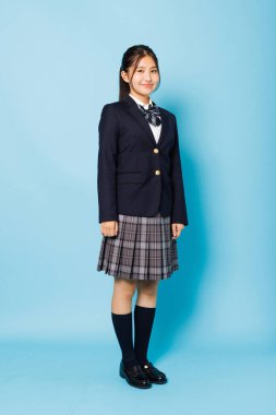 Mavi arka planda kameraya gülümseyen mutlu Japon öğrenci portresi.