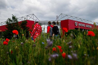 Mainz, Almanya - 17 Mayıs 2025: Futbol taraftarları Mewa ArENA 'ya doğru yürüyorlar. FSV Mainz 05, renkli çiçek tarlalarının arkasında görüldü. Bundesliga eşleşmesi öncesinde manzaralı atmosfer oluşturuluyor.