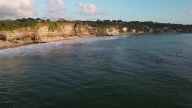 Bali uçurumuna bakan okyanusta gün batımında sörfçüler okyanusta bir dalga yakalarlar. Havadan güneşin ve okyanusun gün batımına doğru fırlatılıyor. Aktif spor ve ekstrem spor kavramı.
