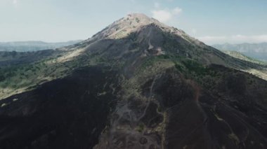 Bali 'deki Batur volkanının kuş bakışı görüntüsü. Volkanın üstündeki siyah lav ve motosiklet izleri. Tırmanmak için dağ yolları, dağların güzel manzarası..