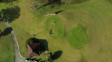 Arkadaşlar hafta sonunu golf oynayarak geçirirler. Bir adamın golf topuna vurup topun deliğe vuruşunu izlediği hava görüntüsü. Yeşil çimenlikteki bir golf kulübünde bir grup insanı vurmak..