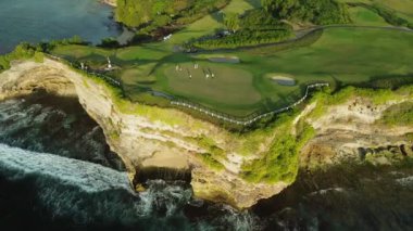 Okyanus kıyısındaki bir uçuruma tünemiş golf oynayan bir grup insanın insansız hava aracı görüntüleri. Sahilde yeşil golf sahası var, insanlar golf oynuyor. Yüksek kalite 4k görüntü.