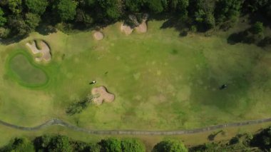 Aile tatili golf oynuyor. Golf sahalarında uçan iki golf arabası hareket ediyor. Yeşil arazi manzarası, golf kulübü tatili. Bir İHA 'nın üzerinden arabaların arkasından geçerek..