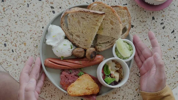 Traditional British breakfast in a plate taken by a man. A close shot of male hands taking a plate of traditional breakfast which includes eggs Benedict, fried sausages, bacon, and toast.