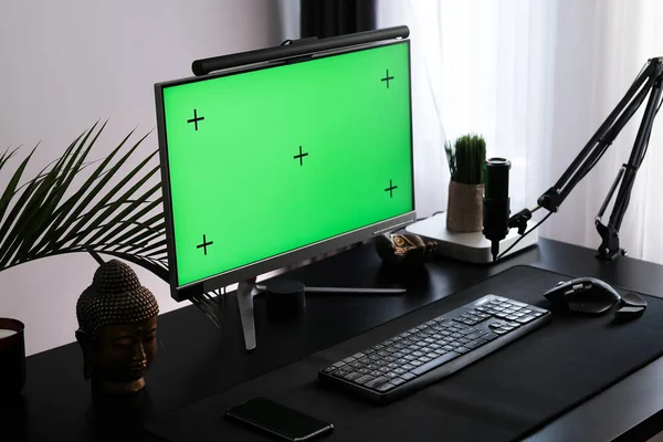 Workspace, monitor with chromakey. Green monitor screen in a modern apartment interior. Computer and microphone, workplace of a gamer, streamer, and podcast host.