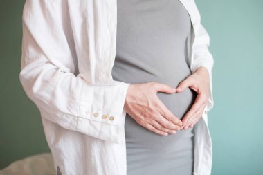 Hamileliğinin son ayında büyük bir göbeği olan hamile bir kadın. Hamile karnının üzerinde ellerini kalp şeklinde katlayan kadın. Bir annenin bebeğine olan sevgisi ve bakımı. Mutlu annelik.