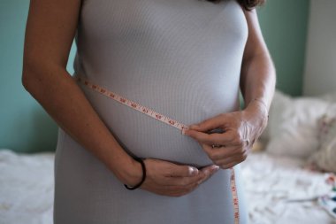 Hamileliğin jinekolojik muayenesi. Hamile bir kadın geniş karnının hacmini 2,5 cm 'lik bir bant ile ölçer. Hamilelik sırasında ağırlık kontrolü.