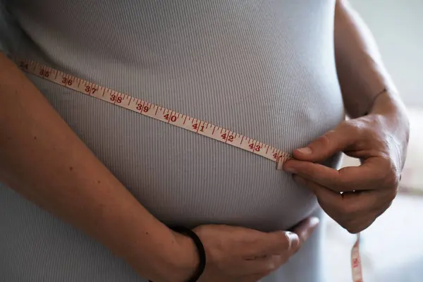Close-up of a pregnant womans big belly, measuring her belly with an inch tape. Weight gain during pregnancy, monitoring the health of a pregnant woman.