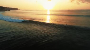 Gün batımında okyanusun yukarıdan görünen görüntüsü, sörfçülerin büyük dalgaları yakaladığı. Bir grup sörfçü sırada dalgaların yükselmesini bekliyor. Dalgaların yükselmesini bekliyorlar. Gün batımında sörf, altın saat.