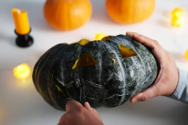 A close-up view of the hands of a man preparing the decorations for Halloween. A man carves a scary face on a pumpkin and uses a knife to cut out the mouth of the pumpkin. Preparing for the Halloween.