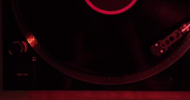Vinil bir plağın döndüğü vinil bir pikabın yukarıdan aşağı görüntüsü. Plak plağında stil olan bir tonearm ve müzik çalarken üzerinden kayıyor. Kırmızı ışık geçmişe dönük.